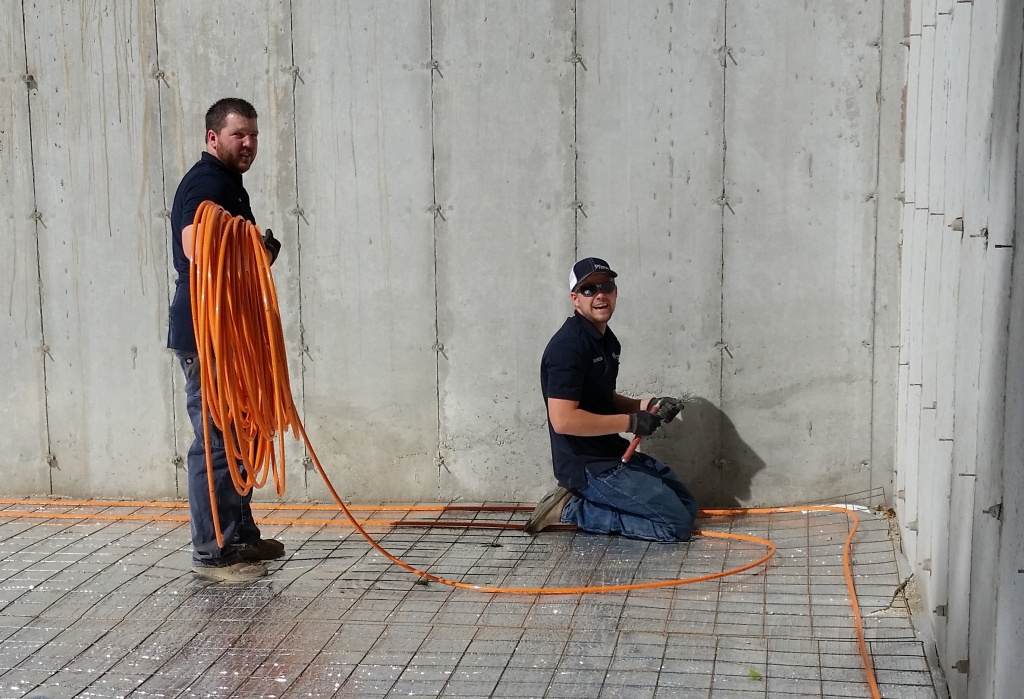 Two men working on concrete wall with orange hose.