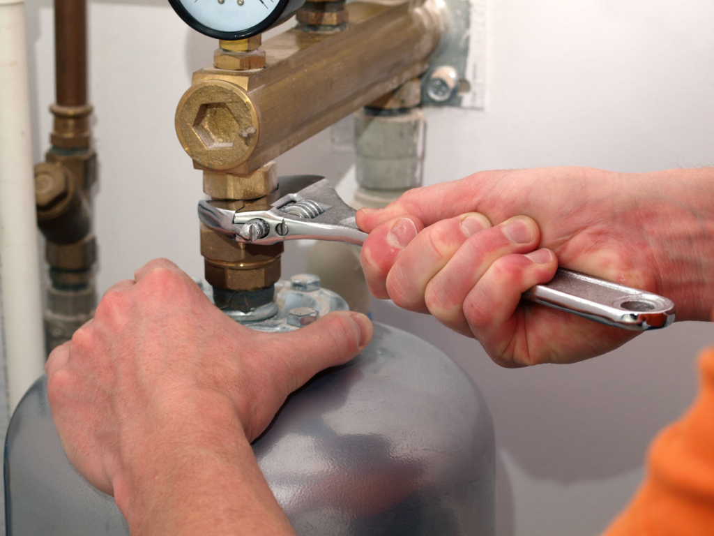 A person using a wrench to adjust a water heater.