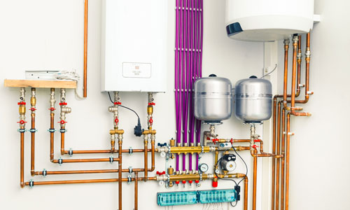A white wall with pipes and water heaters. Providing boilers and radiant heat system services.