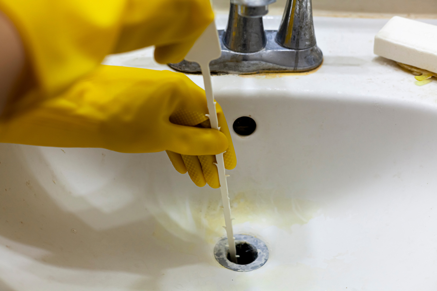 Person in yellow rubber gloves cleaning a sink with drain cleaning products.