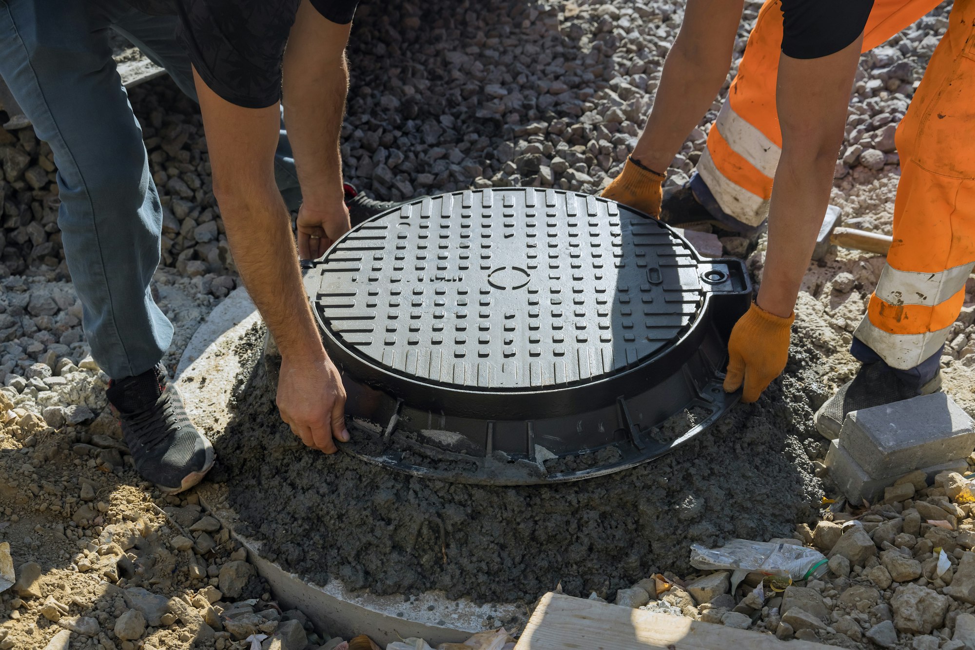 Two men with gloves are working on a manhole cover.