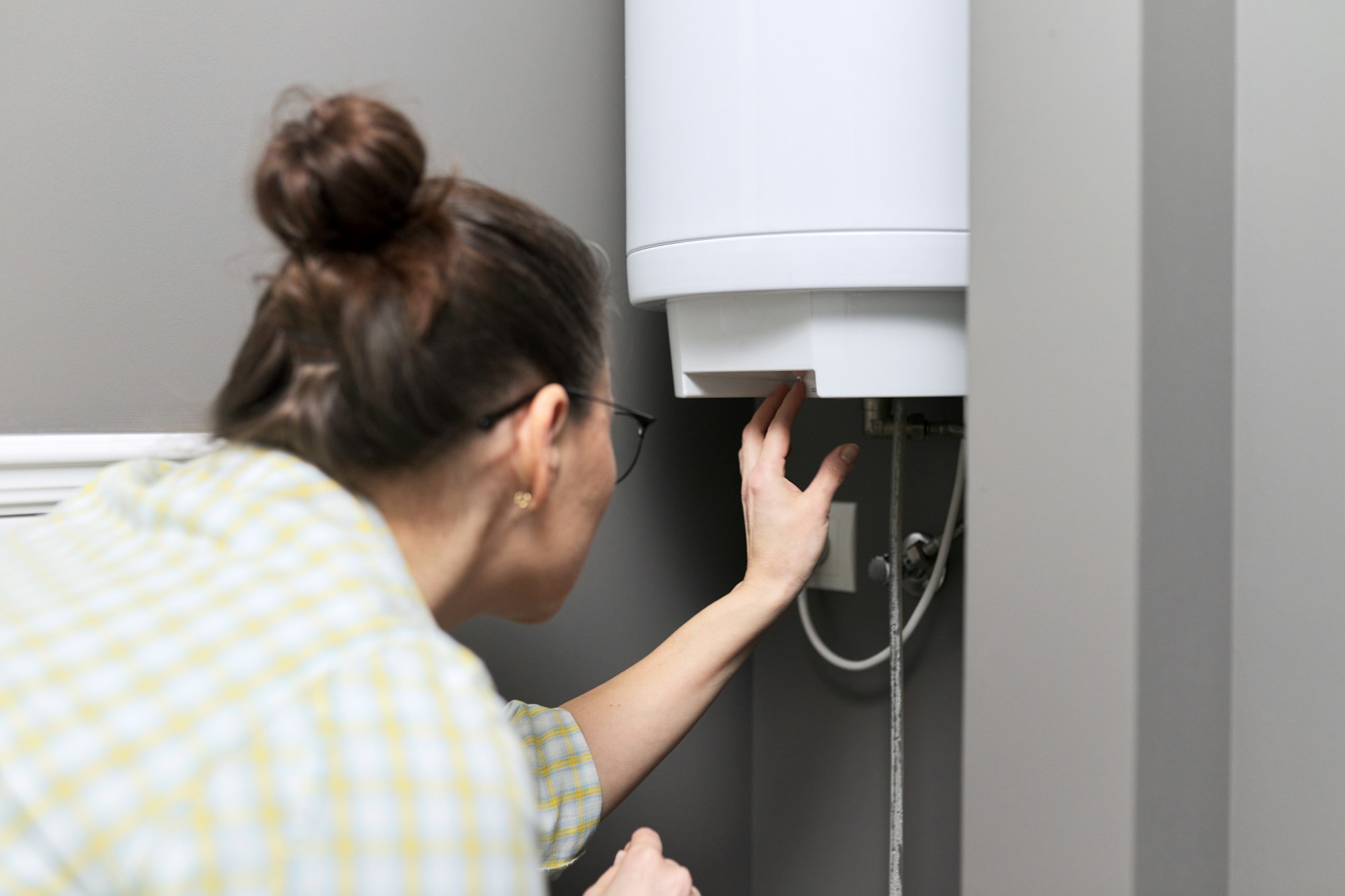 A woman repairs a water heater in a bathroom, showcasing her skills as a professional plumber