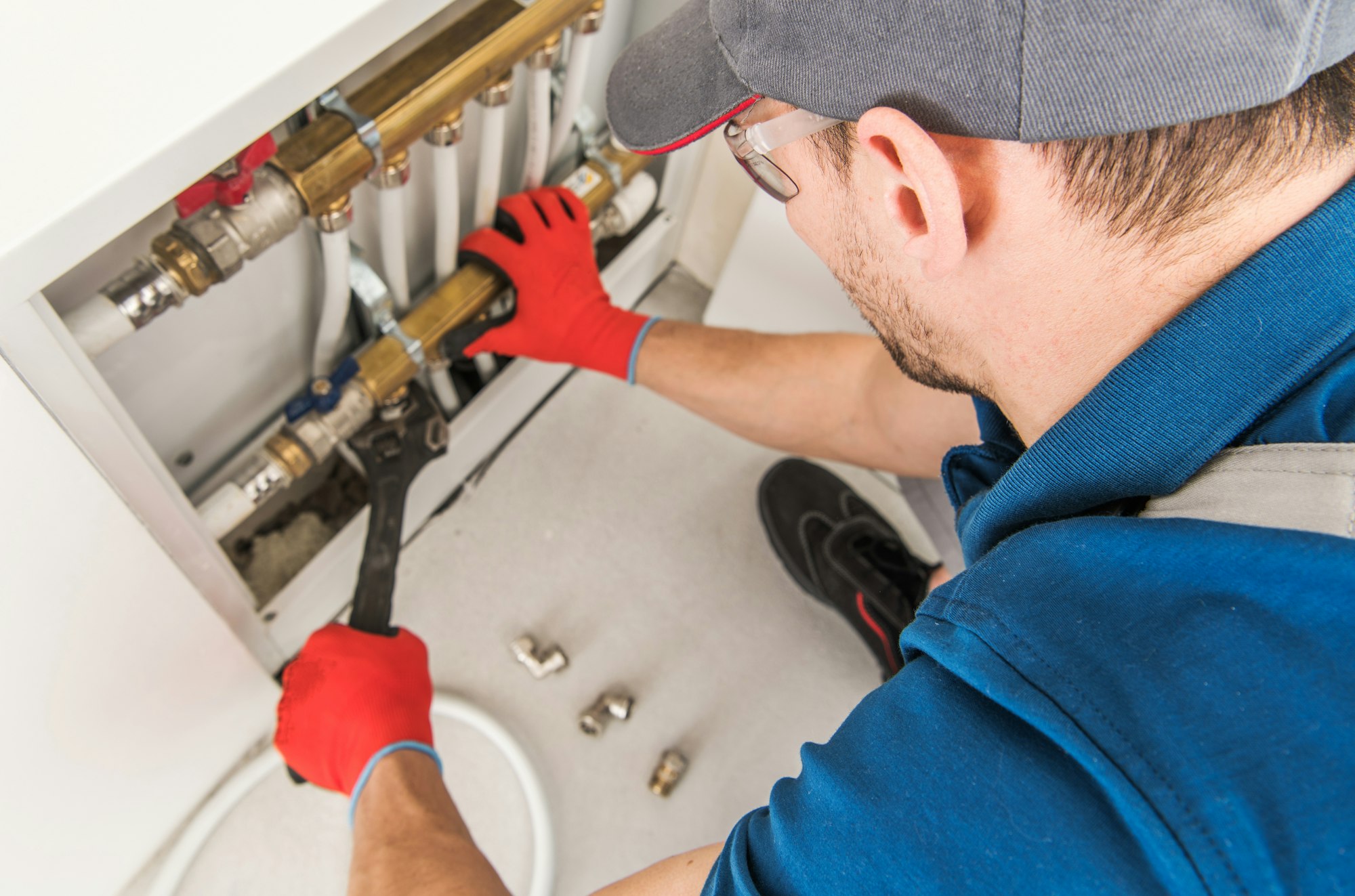 A man fixing a metal sink with a pipe and wrench.