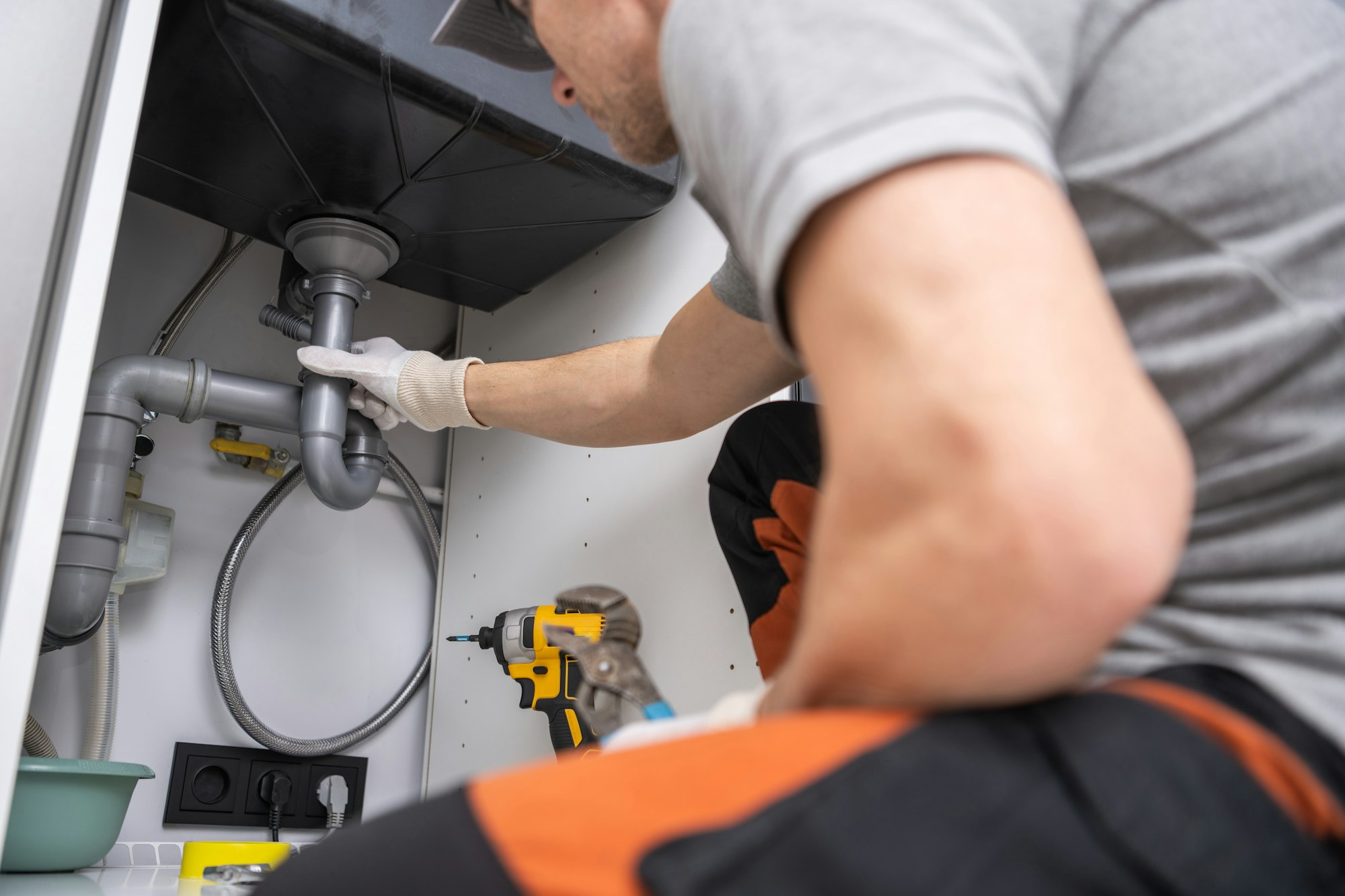 A man fixing a metal sink with a pipe and wrench.
