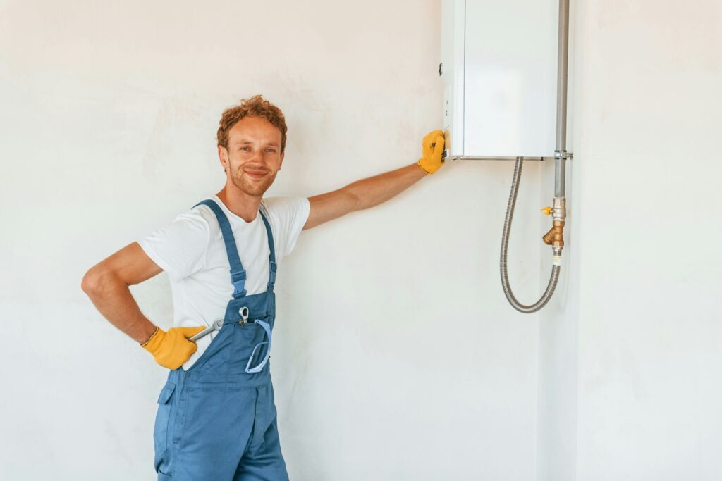 A man in overalls stands next to a water heater, representing a scene of home repair and maintenance.