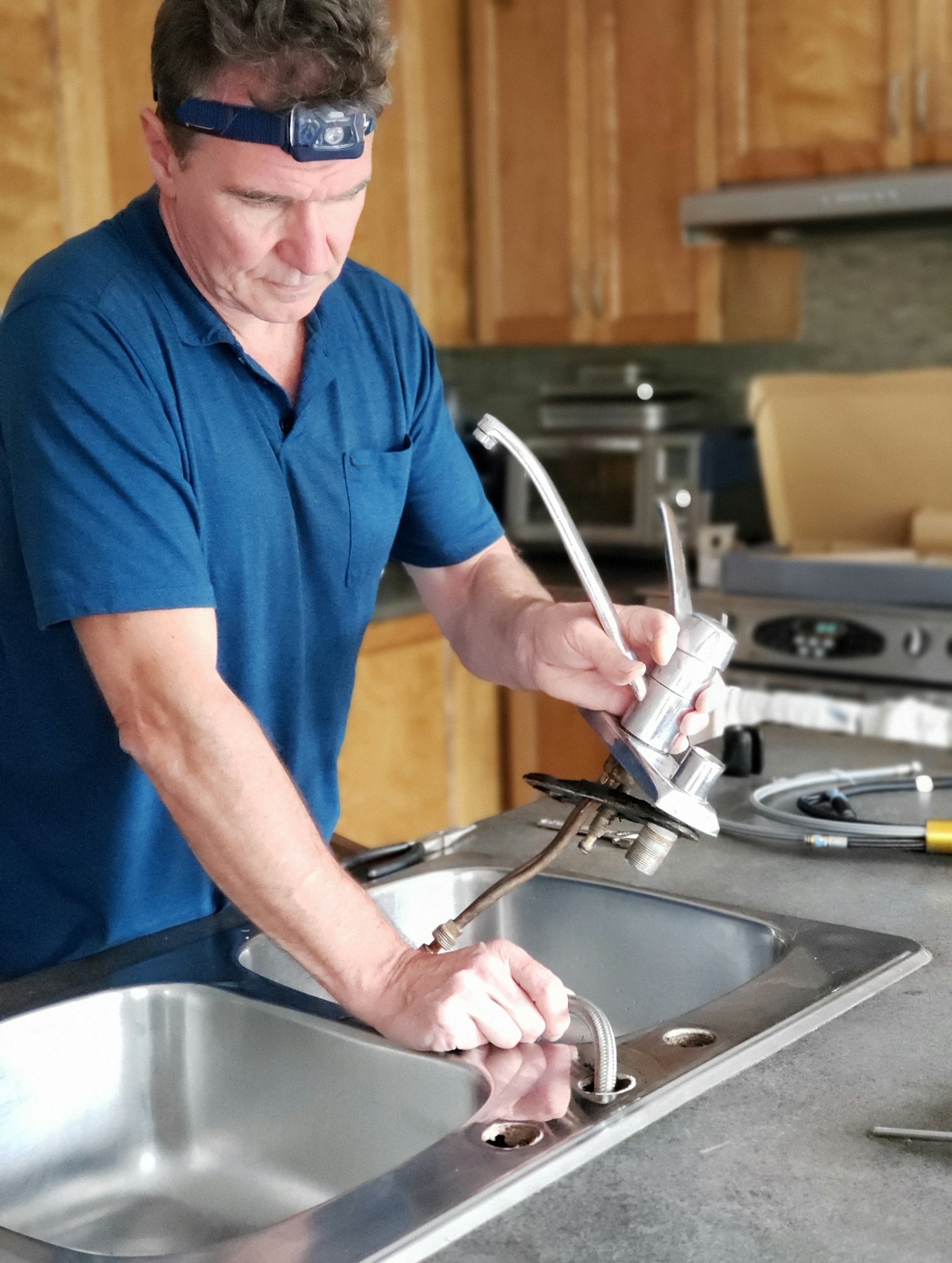 A man is diligently repairing a kitchen sink faucet, representing the quality service of PPS Plumbing.