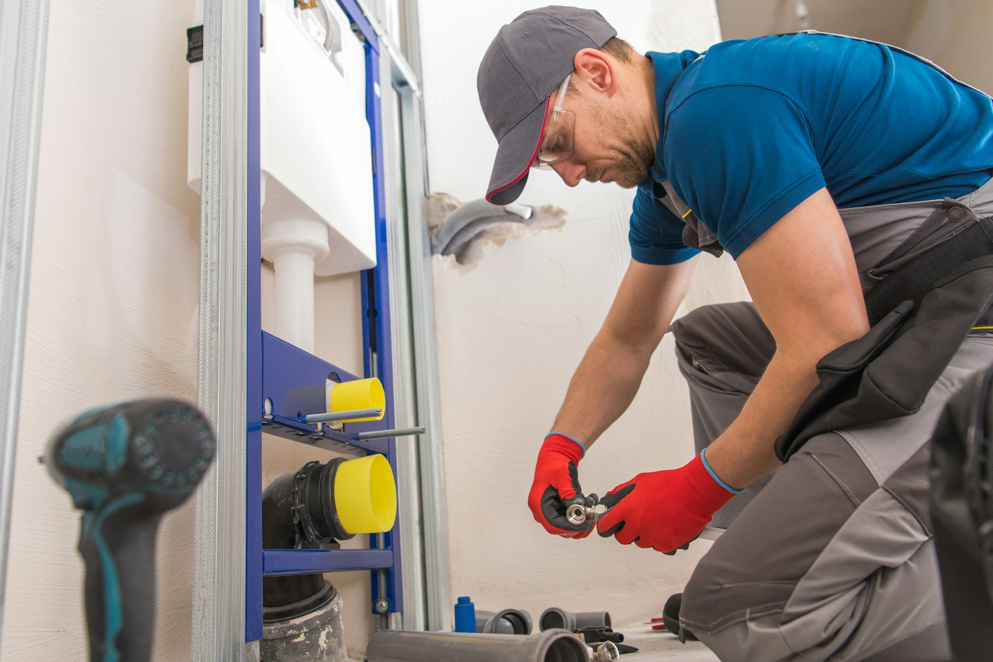 A plumber in a blue shirt and red gloves fixing a toilet.